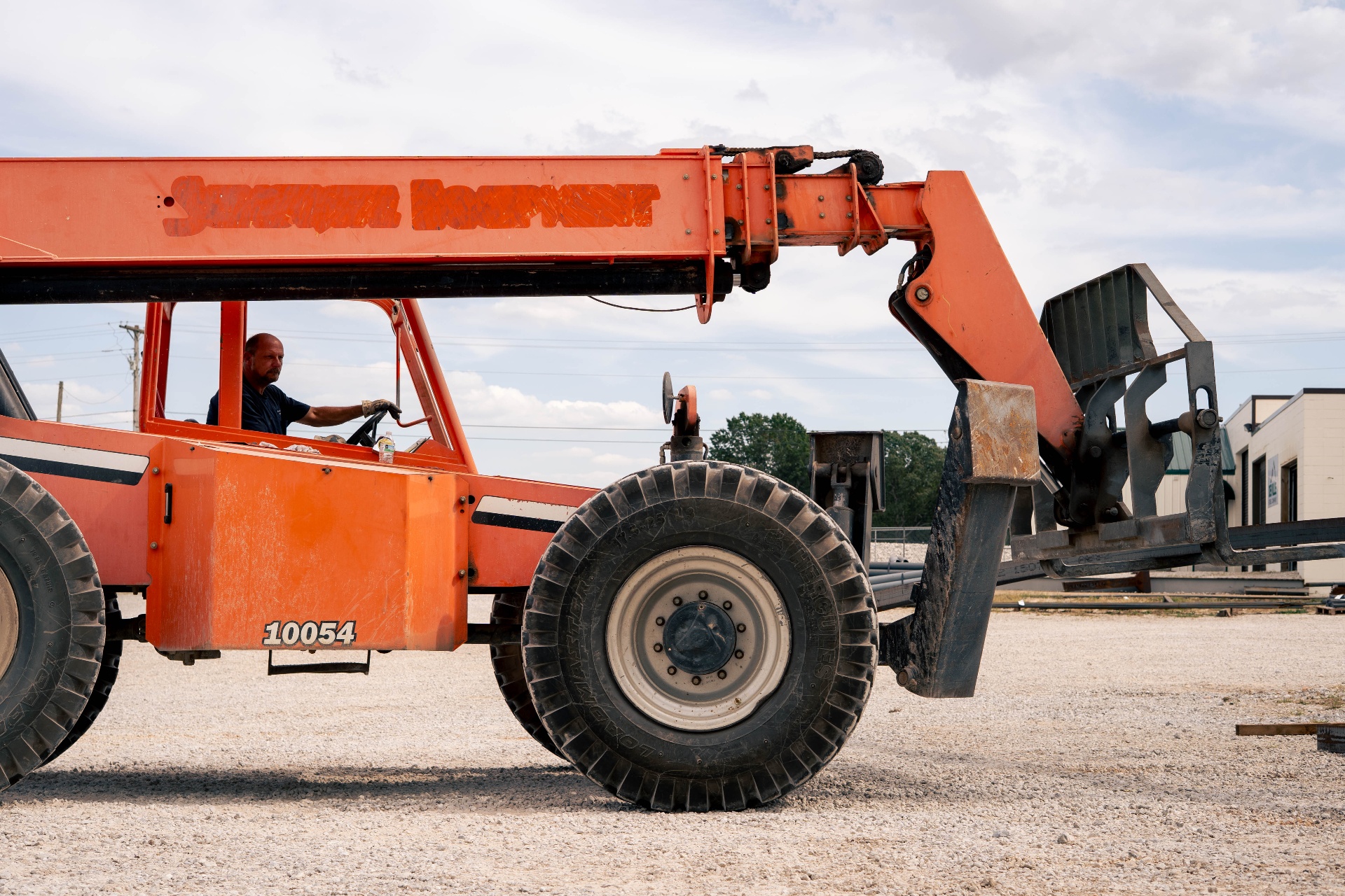 Operator maneuvering an orange telehandler in the yard